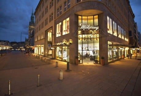 Edifício comercial em rua de pedestres ao anoitecer, com vitrines iluminadas no térreo