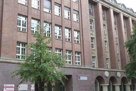 Brick facade of a large office building with arched arcades on the ground floor and a tree in front