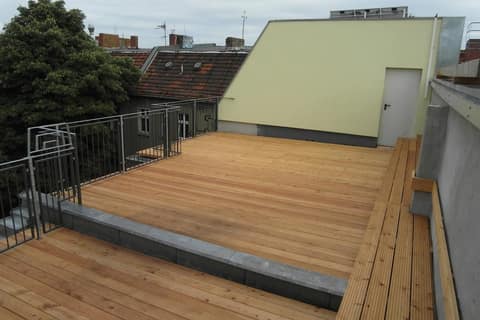 Completed roof terrace with light timber decking and a bench along the parapet, Berlin rooftops all around