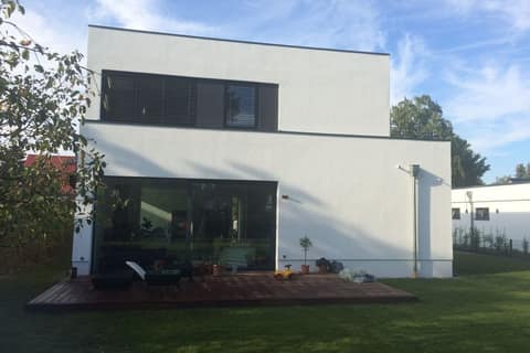 Garden side of a two-storey white flat-roofed house with a timber terrace and seating in front