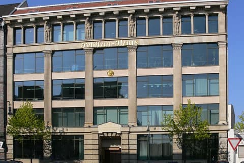 Historic stone facade of an office building with tall pilasters, sculptural figures on the top floor and large glazed areas