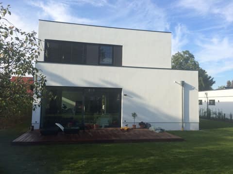 Gartenseite eines zweigeschossigen weißen Hauses mit Flachdach, raumhoher Schiebetür und Holzterrasse