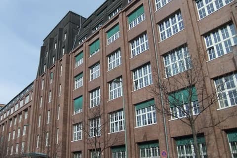 Brick facade of a multi-storey office building with tall multi-pane windows and a dark rooftop extension